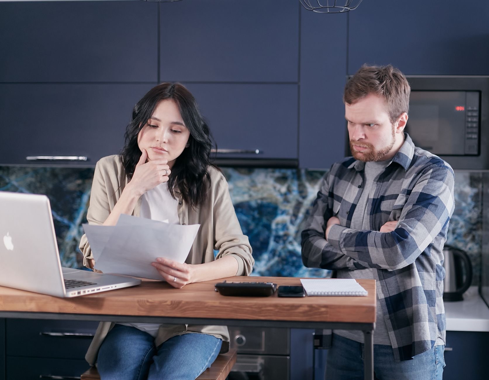 A couple sitting at a kitchen desk reviewing financial documents, using a laptop.